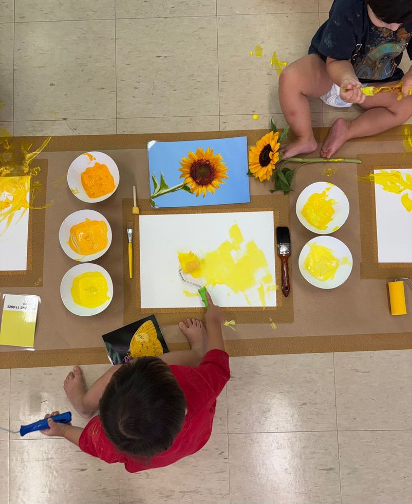 Crianças explorando atividade de pintura com girassóis em sala de arte